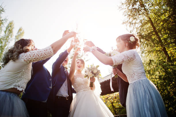Wedding couple and groomsmen with bridesmaids drinking champagne outdoors in the park or garden.